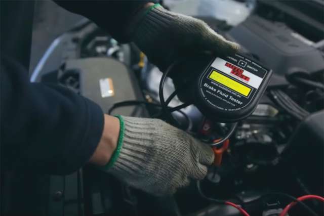 A technician uses an electronic brake fluid tester to gauge the moisture level of the fluid.